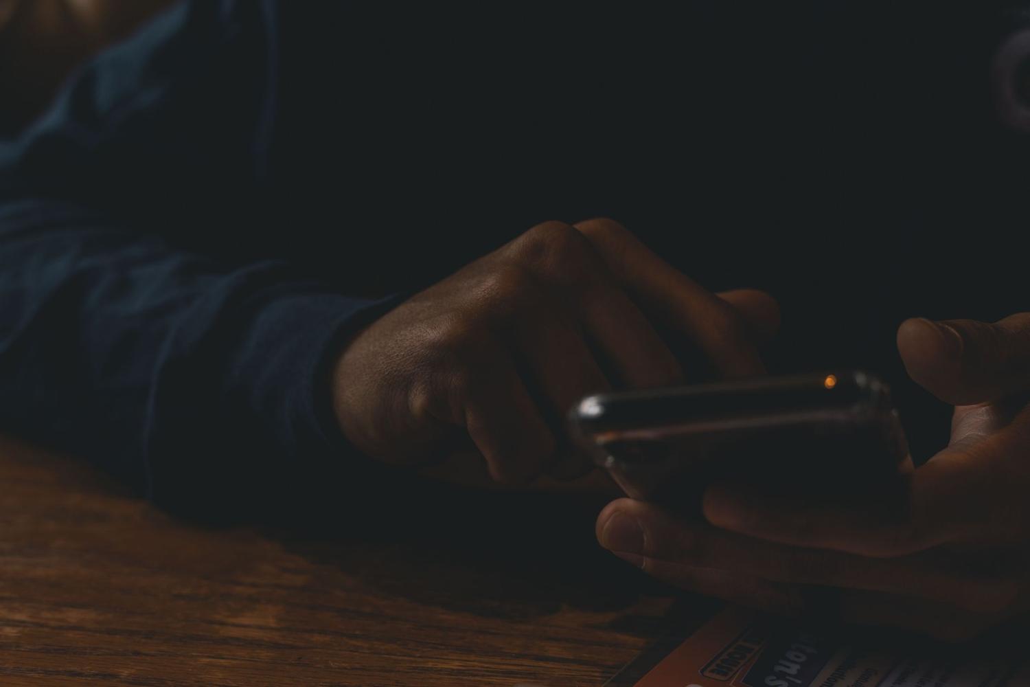 Mãos segurando um celular iluminado em ambiente escuro